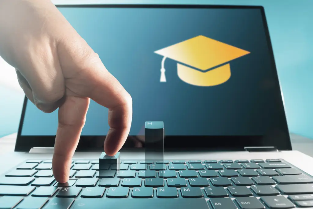 Online Training Courses- A hand using two fingers to walk across a laptop keyboard with a graduation cap icon displayed on the screen.